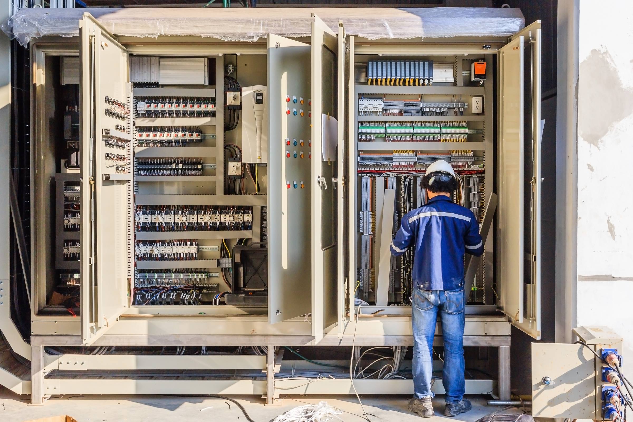 Engineer working inside a large open industrial control cabinet